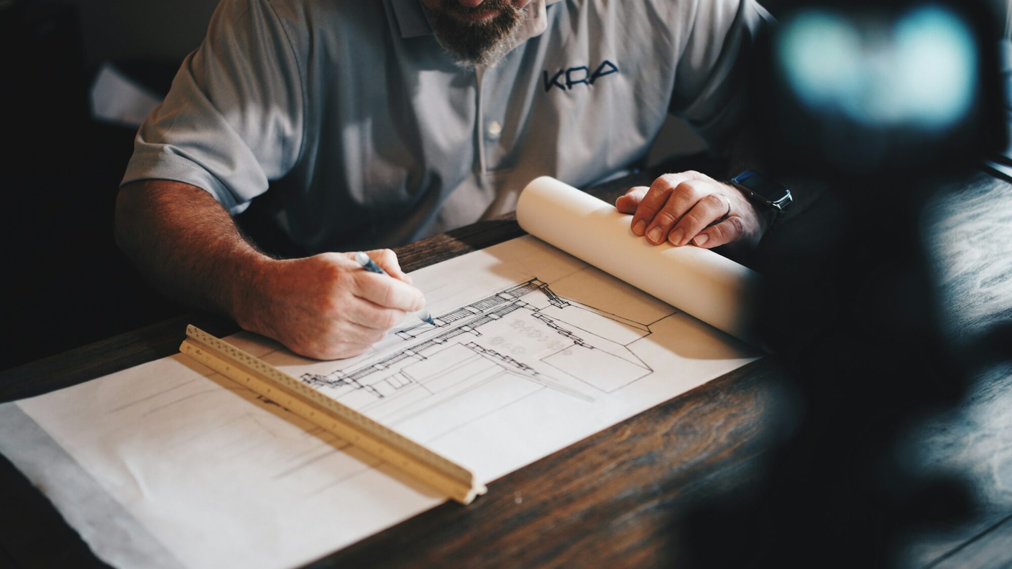 Mano de arquitecto delineando sobre planos en la mesa de trabajo del estudio