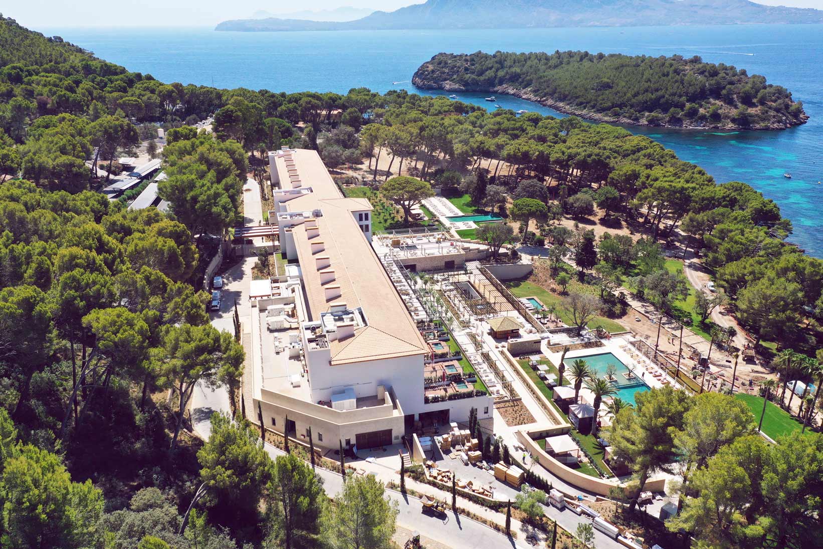 Vista aérea del Four Seasons Resort Mallorca at Formentor: el edificio blanco entre el pinar, con la cala y la bahía de Pollença al fondo